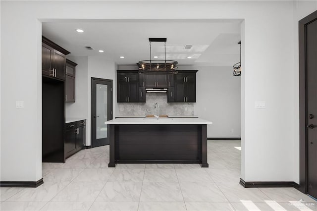 kitchen featuring a center island with sink, an inviting chandelier, sink, and tasteful backsplash