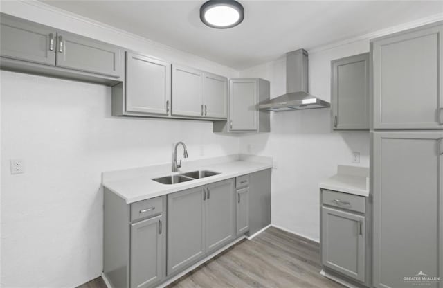 kitchen with gray cabinets, light hardwood / wood-style flooring, sink, and wall chimney exhaust hood