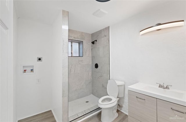 bathroom with tiled shower, hardwood / wood-style flooring, vanity, and toilet