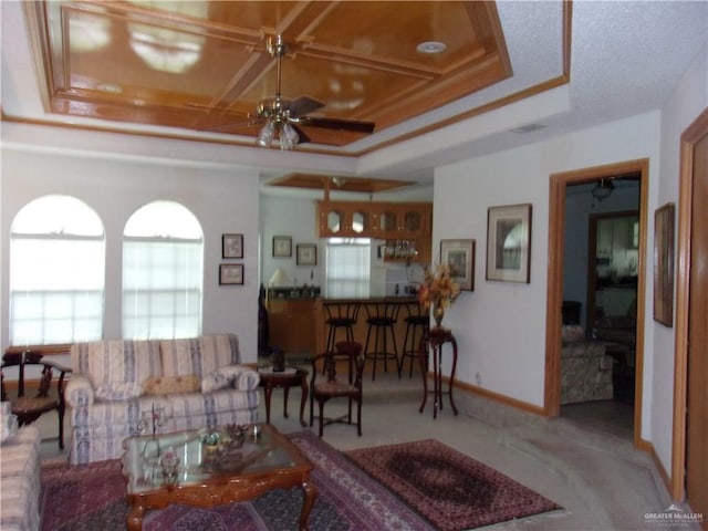 carpeted living room with ceiling fan, crown molding, and a tray ceiling