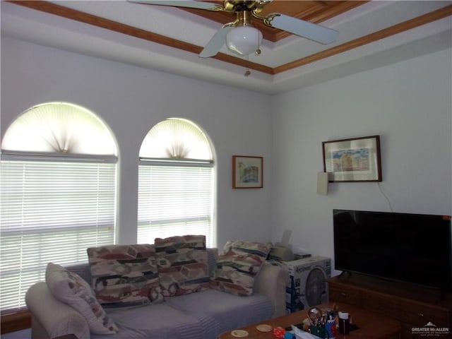 living room with ceiling fan, a raised ceiling, and crown molding