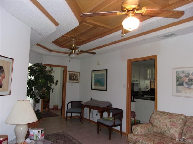 tiled living room featuring a raised ceiling, ceiling fan, and ornamental molding