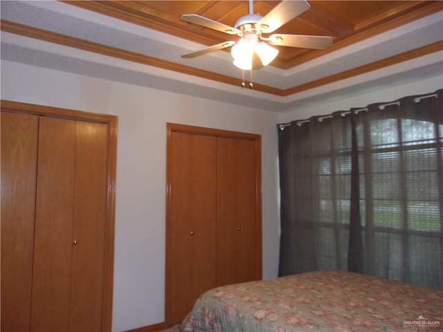 bedroom featuring two closets, ceiling fan, ornamental molding, and a tray ceiling