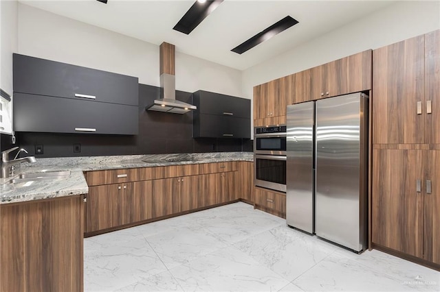 kitchen featuring marble finish floor, a sink, appliances with stainless steel finishes, wall chimney range hood, and light stone countertops