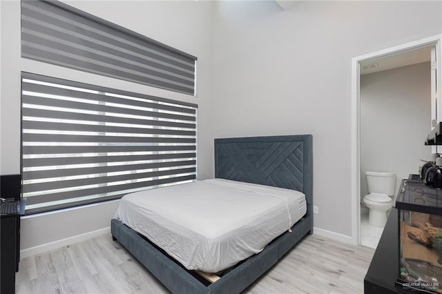 bedroom with connected bathroom, baseboards, and wood finished floors