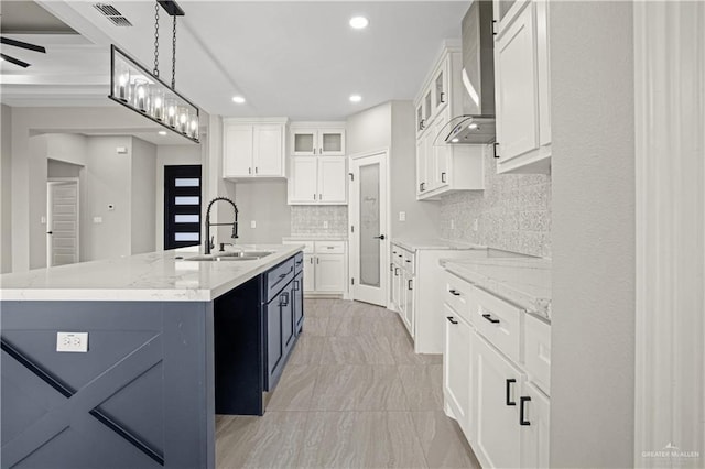 kitchen with pendant lighting, a kitchen island with sink, sink, wall chimney exhaust hood, and white cabinetry