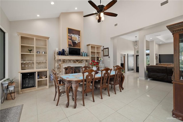 tiled dining space featuring a stone fireplace, ceiling fan, and high vaulted ceiling