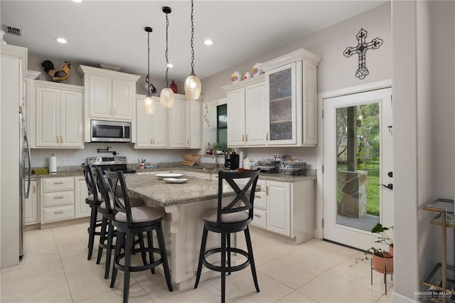 kitchen featuring a center island, a kitchen breakfast bar, light stone counters, white cabinetry, and stainless steel appliances