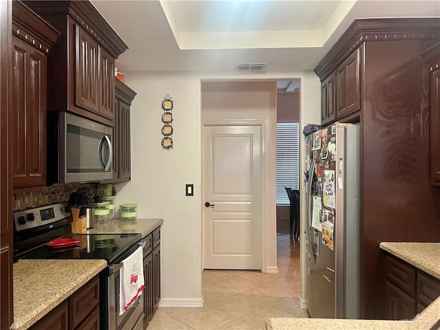 kitchen featuring light tile patterned floors, stainless steel appliances, dark brown cabinetry, a tray ceiling, and decorative backsplash