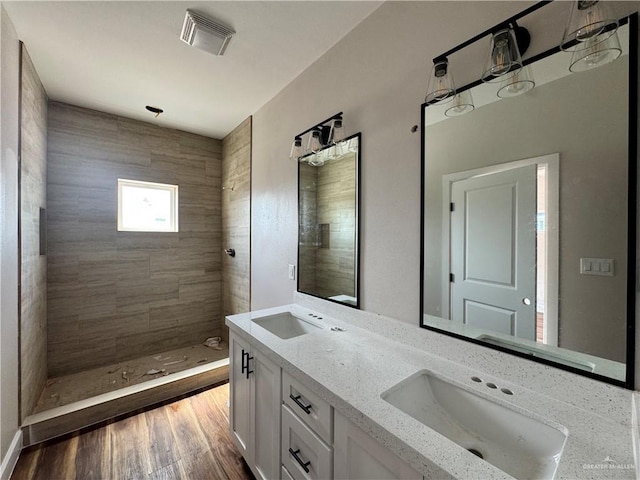 bathroom with wood finished floors, visible vents, tiled shower, and a sink