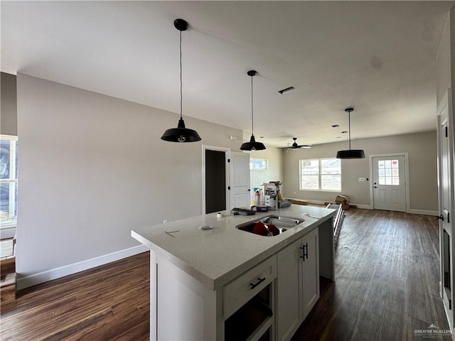 kitchen featuring open floor plan, baseboards, dark wood-style flooring, and a kitchen island with sink