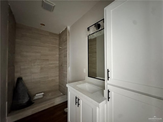 full bathroom featuring visible vents, wood finished floors, vanity, and tiled shower