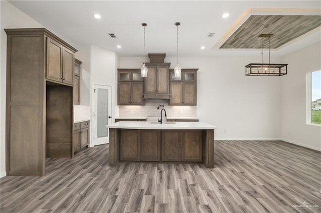 kitchen with wood-type flooring, a kitchen island with sink, hanging light fixtures, and sink