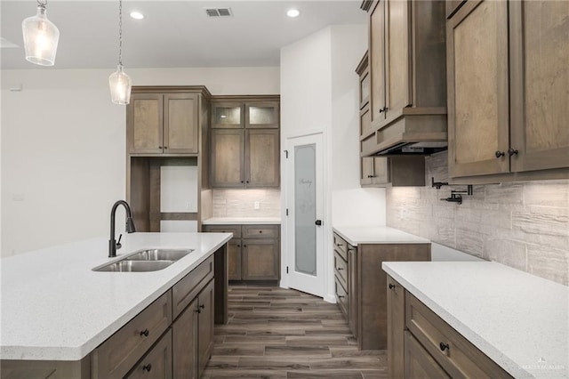 kitchen with pendant lighting, backsplash, dark wood-type flooring, sink, and light stone countertops