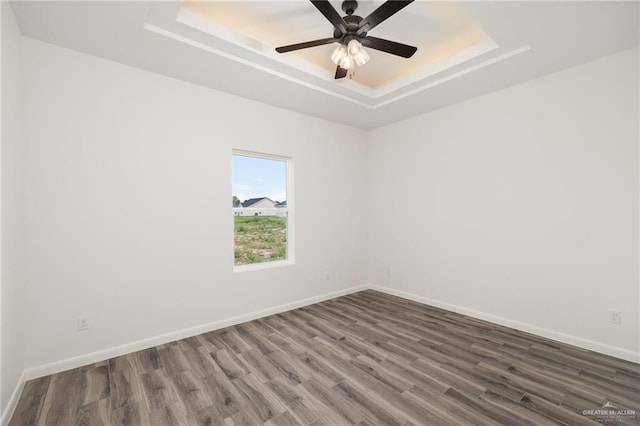 empty room featuring ceiling fan, dark hardwood / wood-style flooring, and a tray ceiling