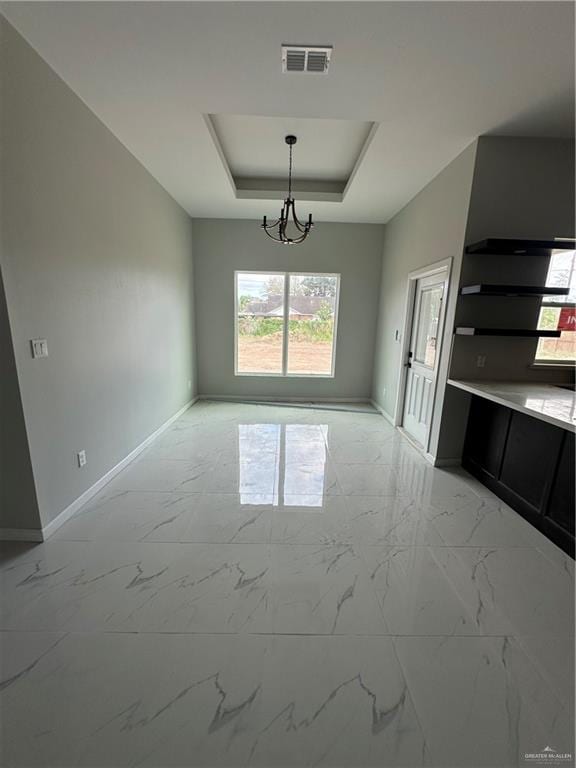 unfurnished dining area with a tray ceiling and an inviting chandelier