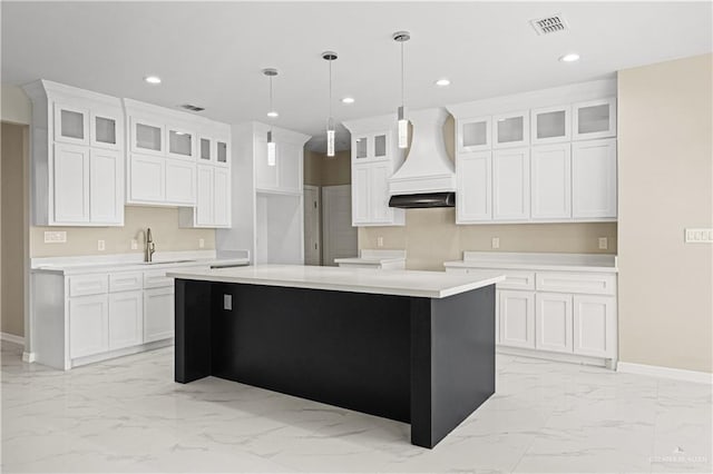 kitchen featuring custom exhaust hood, white cabinetry, and an island with sink