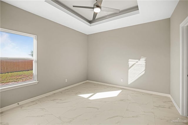 unfurnished room with a tray ceiling, plenty of natural light, and ceiling fan