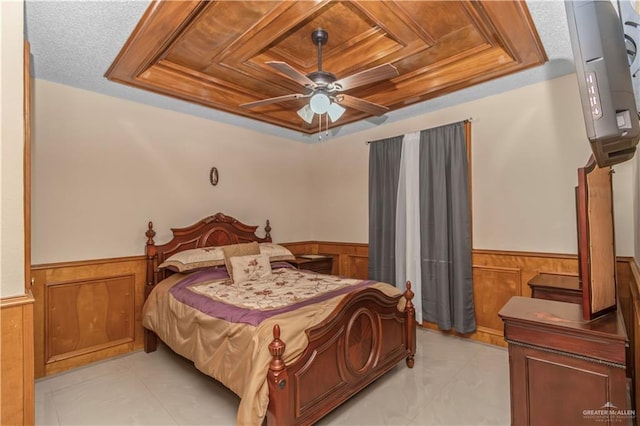 bedroom featuring ceiling fan, a raised ceiling, a textured ceiling, and wooden walls