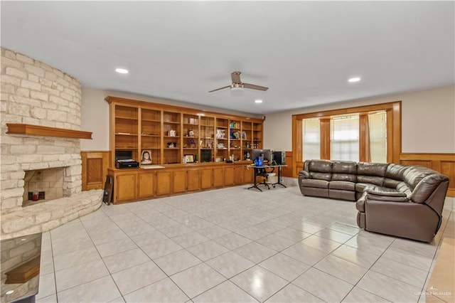 tiled living room with ceiling fan and a stone fireplace