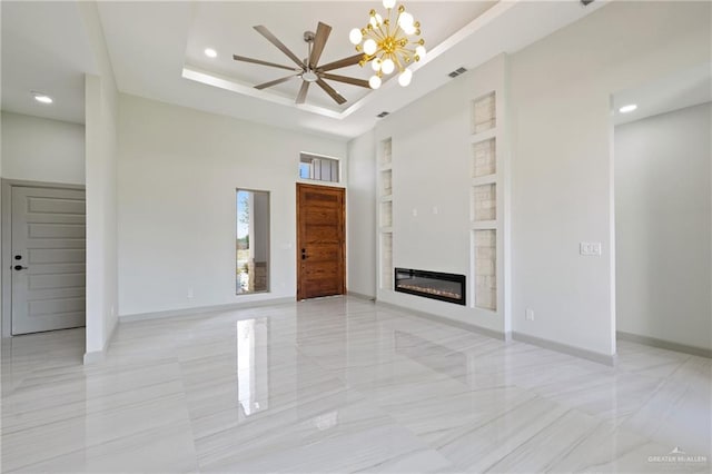 unfurnished living room with recessed lighting, a tray ceiling, a glass covered fireplace, and ceiling fan with notable chandelier