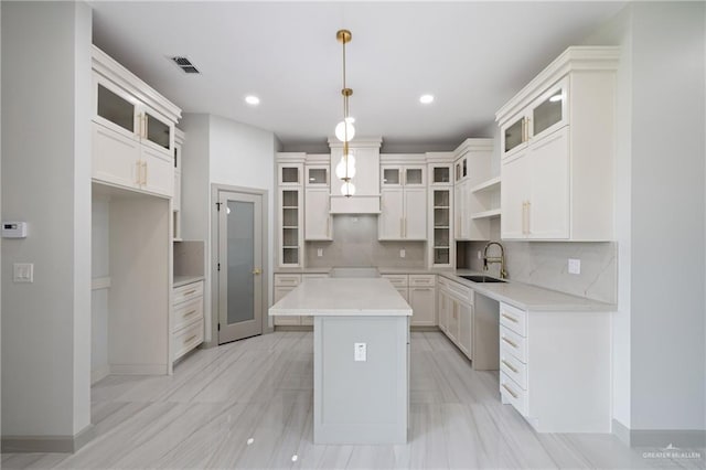 kitchen featuring a sink, tasteful backsplash, a kitchen island, visible vents, and glass insert cabinets