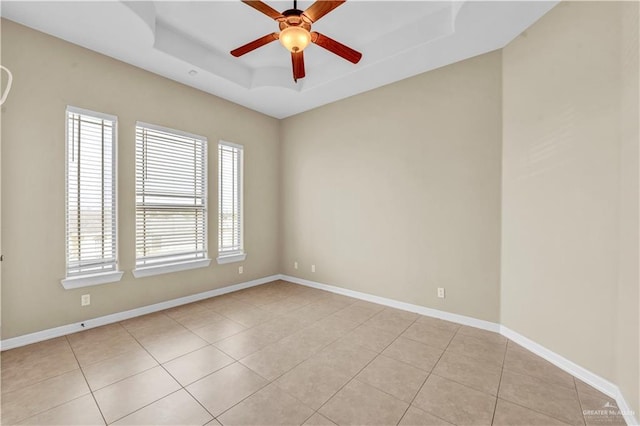 unfurnished room with a tray ceiling, light tile patterned flooring, a ceiling fan, and baseboards