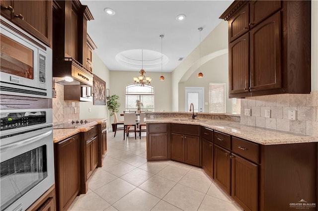 kitchen featuring light stone countertops, a sink, appliances with stainless steel finishes, a raised ceiling, and a notable chandelier