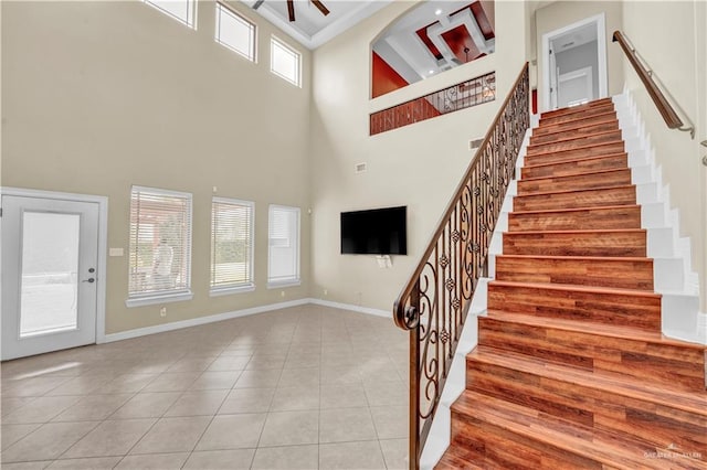 stairs with baseboards, a high ceiling, ceiling fan, and tile patterned flooring