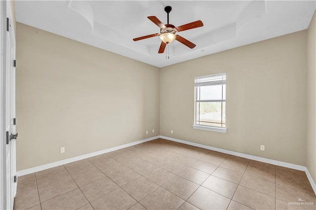 empty room with a raised ceiling, light tile patterned floors, baseboards, and ceiling fan