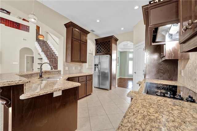 kitchen featuring stainless steel fridge with ice dispenser, light tile patterned floors, arched walkways, black electric cooktop, and a sink