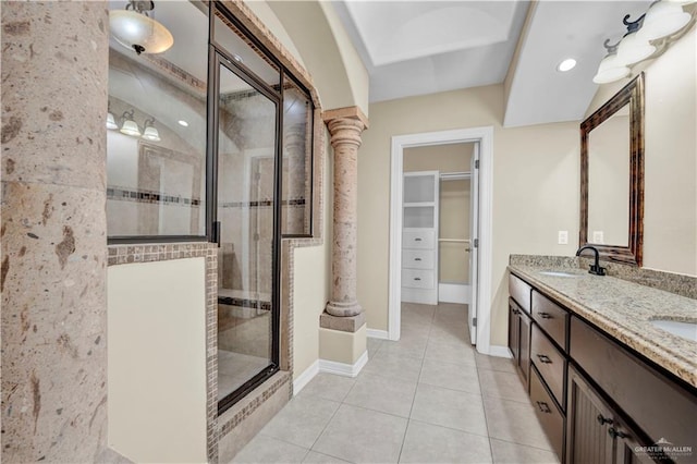 bathroom with a shower stall, a walk in closet, double vanity, tile patterned floors, and a sink