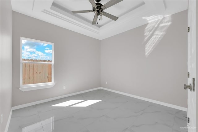 unfurnished room with marble finish floor, ceiling fan, baseboards, and a raised ceiling