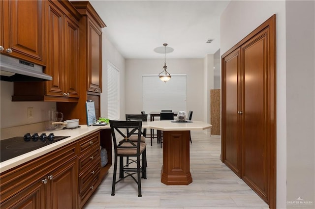 kitchen with black gas stovetop, pendant lighting, a kitchen breakfast bar, and light hardwood / wood-style floors