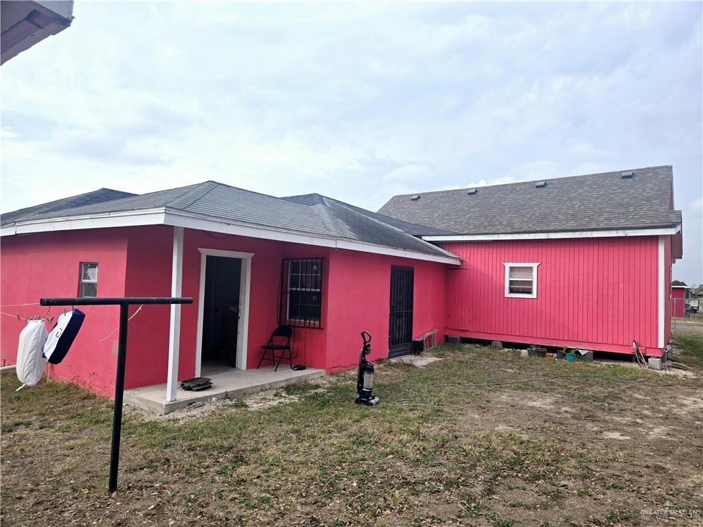 rear view of property with a shingled roof, a patio area, and a yard