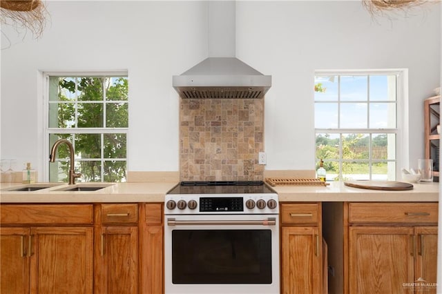 kitchen featuring sink, stainless steel stove, backsplash, and wall chimney range hood