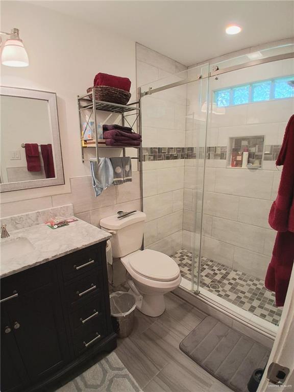 613 W Sprague St, Edinburg, TX 78539 - bathroom featuring vanity, a shower stall, toilet, wood finished floors, and tile walls