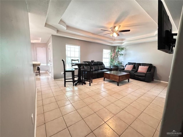 tiled living room with a tray ceiling and ceiling fan