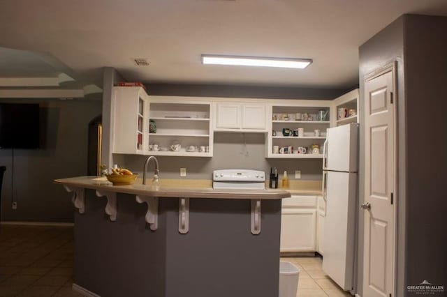 kitchen with white appliances, sink, light tile patterned floors, a kitchen bar, and white cabinetry