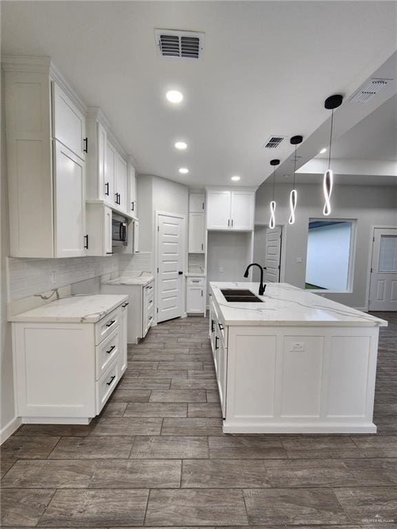 kitchen featuring hanging light fixtures, sink, white cabinets, and an island with sink