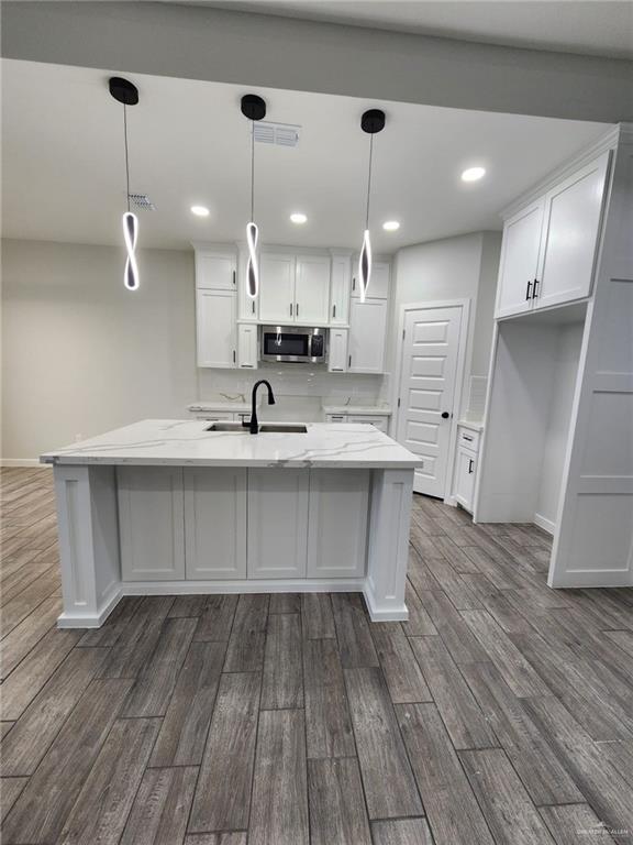 kitchen with white cabinetry, sink, dark wood-type flooring, hanging light fixtures, and light stone counters