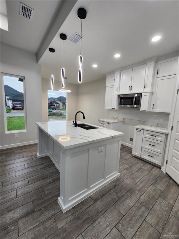 kitchen with white cabinets, decorative light fixtures, a center island with sink, and dark hardwood / wood-style floors