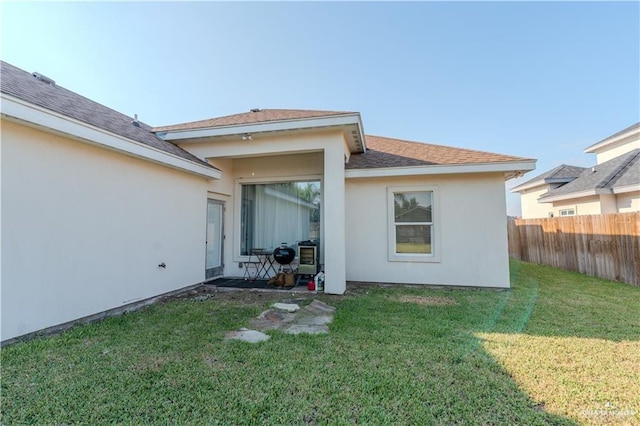 rear view of house with fence, a lawn, and stucco siding