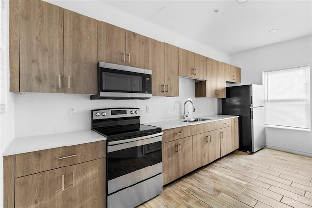 kitchen with backsplash, sink, light wood-type flooring, and appliances with stainless steel finishes