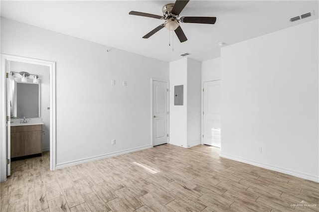 unfurnished bedroom with light wood-type flooring, ensuite bathroom, ceiling fan, sink, and electric panel