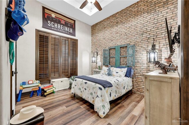 bedroom featuring wood finished floors, brick wall, and a ceiling fan
