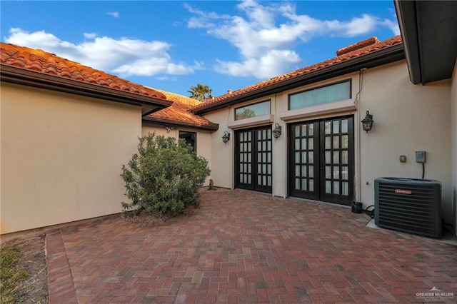 entrance to property featuring french doors, stucco siding, central AC unit, and a tile roof