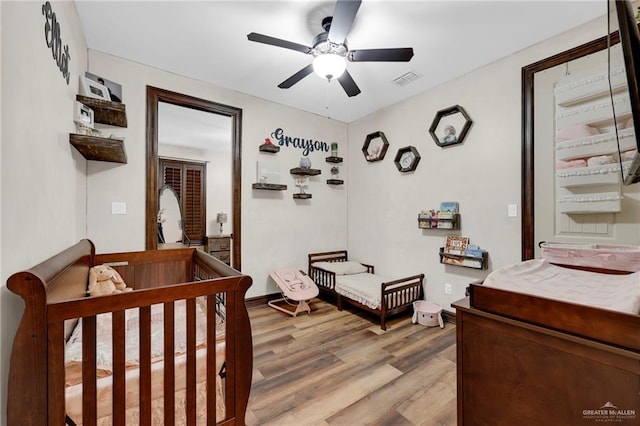 bedroom featuring a crib, light wood finished floors, visible vents, and ceiling fan
