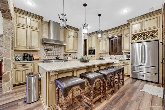 kitchen featuring cream cabinetry, stainless steel refrigerator, built in microwave, and wall chimney range hood