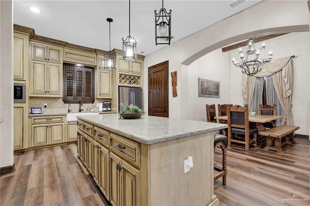 kitchen featuring a chandelier, arched walkways, stainless steel fridge, and cream cabinetry